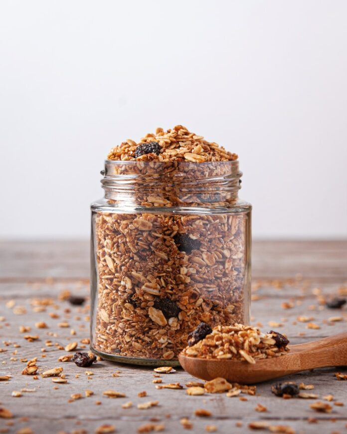 A jar filled with granola next to a wooden spoon