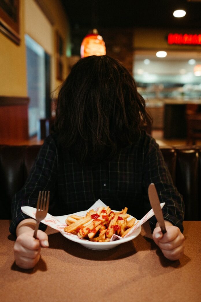 Photo by J E S U S R O C H A woman in black and white plaid long sleeve shirt eating fries